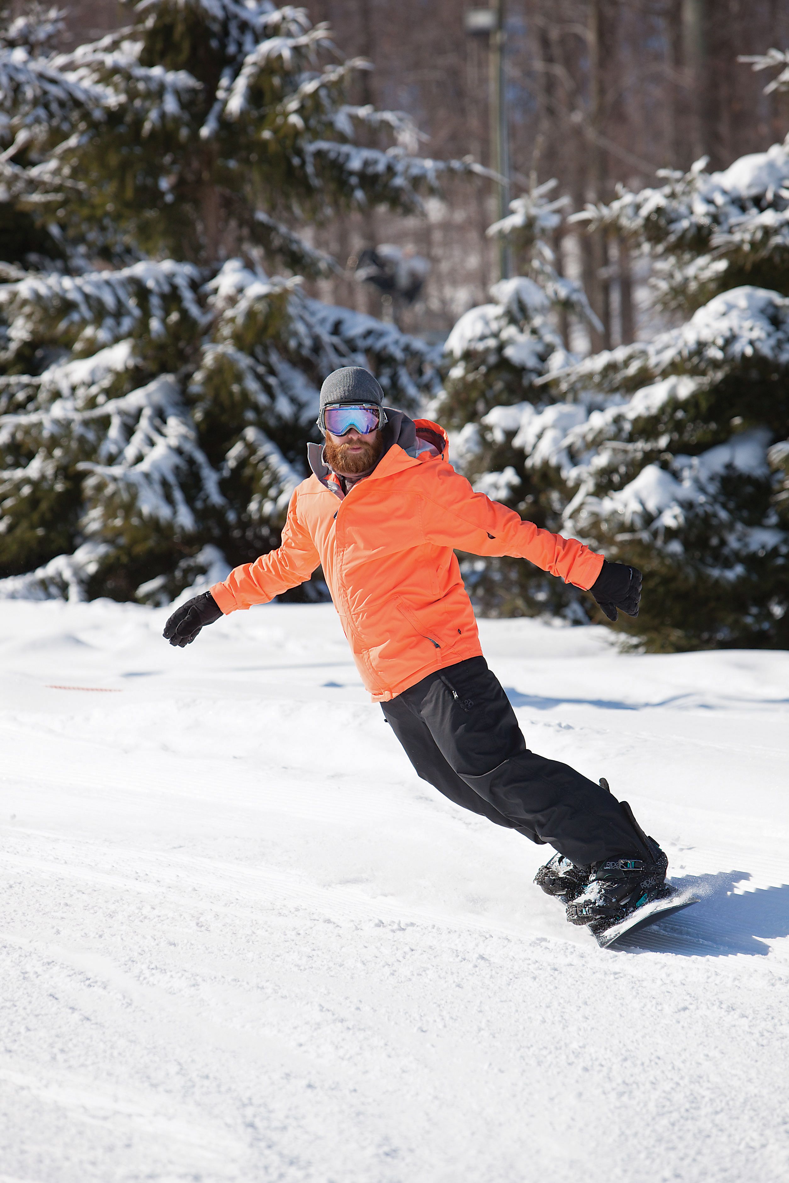 Une personne fait de la planche à neige sur une pente enneigée, avec des arbres en arrière-plan.