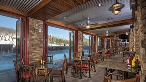 Un restaurante con paredes de piedra, mobiliario de madera y amplios ventanales que dan a un paisaje nevado.