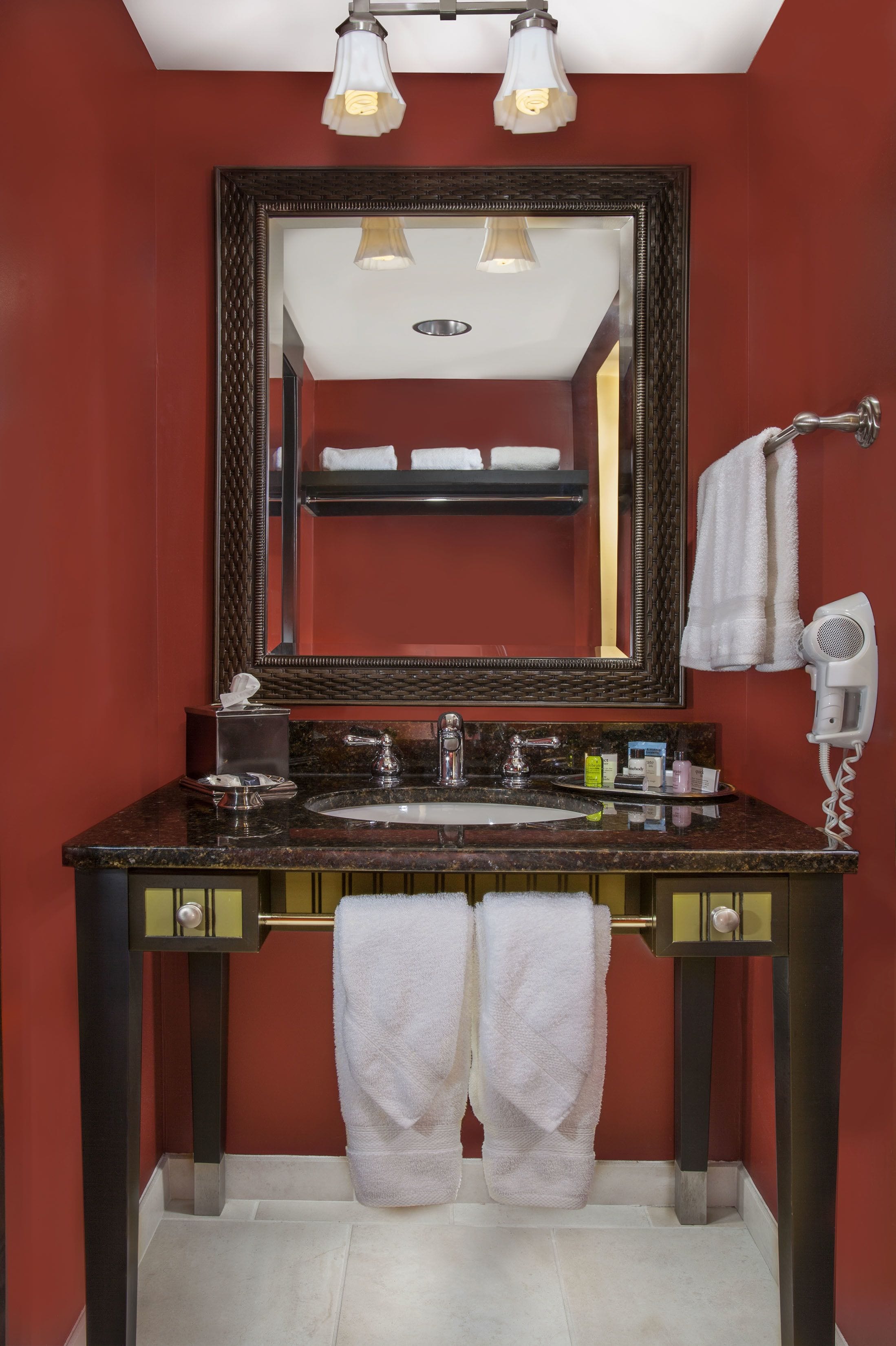 Un baño con un lavamanos de granito oscuro, un espejo grande y un secador de pelo en la pared.