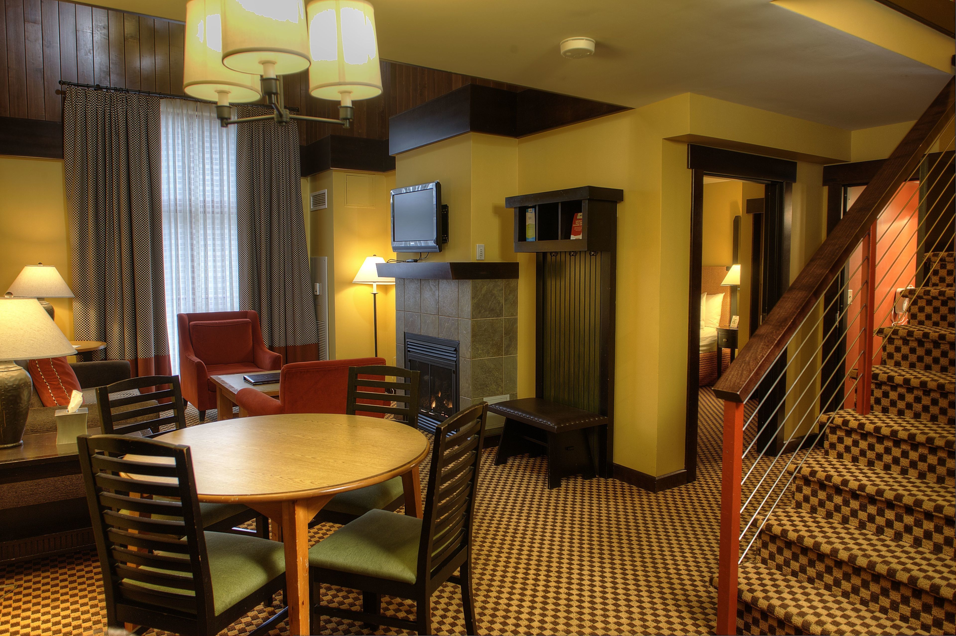 A hotel room with a dining area, a fireplace, a television, and a staircase.