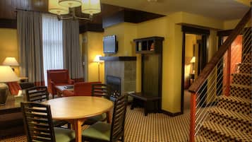 Quarto de hotel com área de refeições, lareira, televisão e escada.
