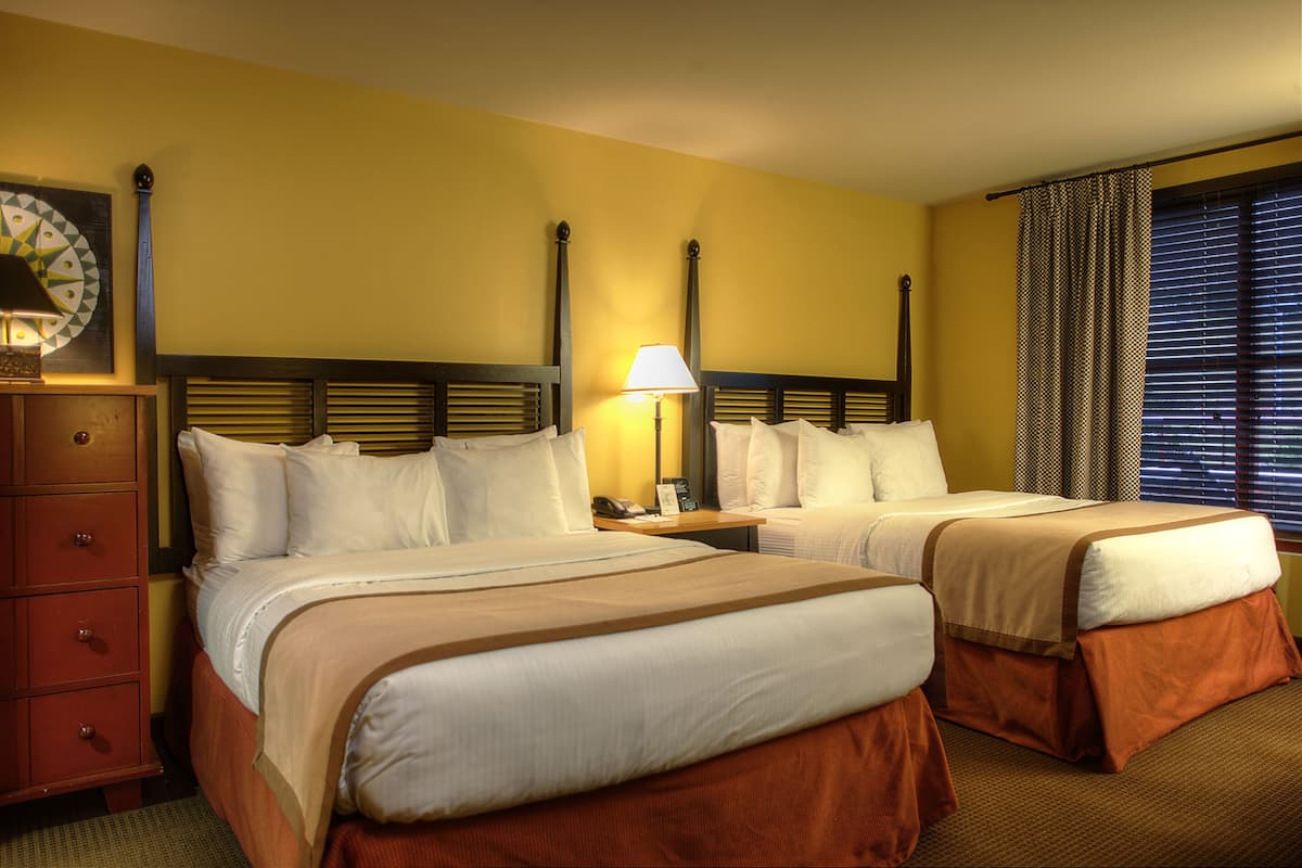 Een hotelkamer met twee bedden, een houten dressoir, een lamp en een raam met jaloezieën.