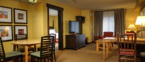 A hotel room with a dining area, a television on a cabinet, and a patterned carpet.