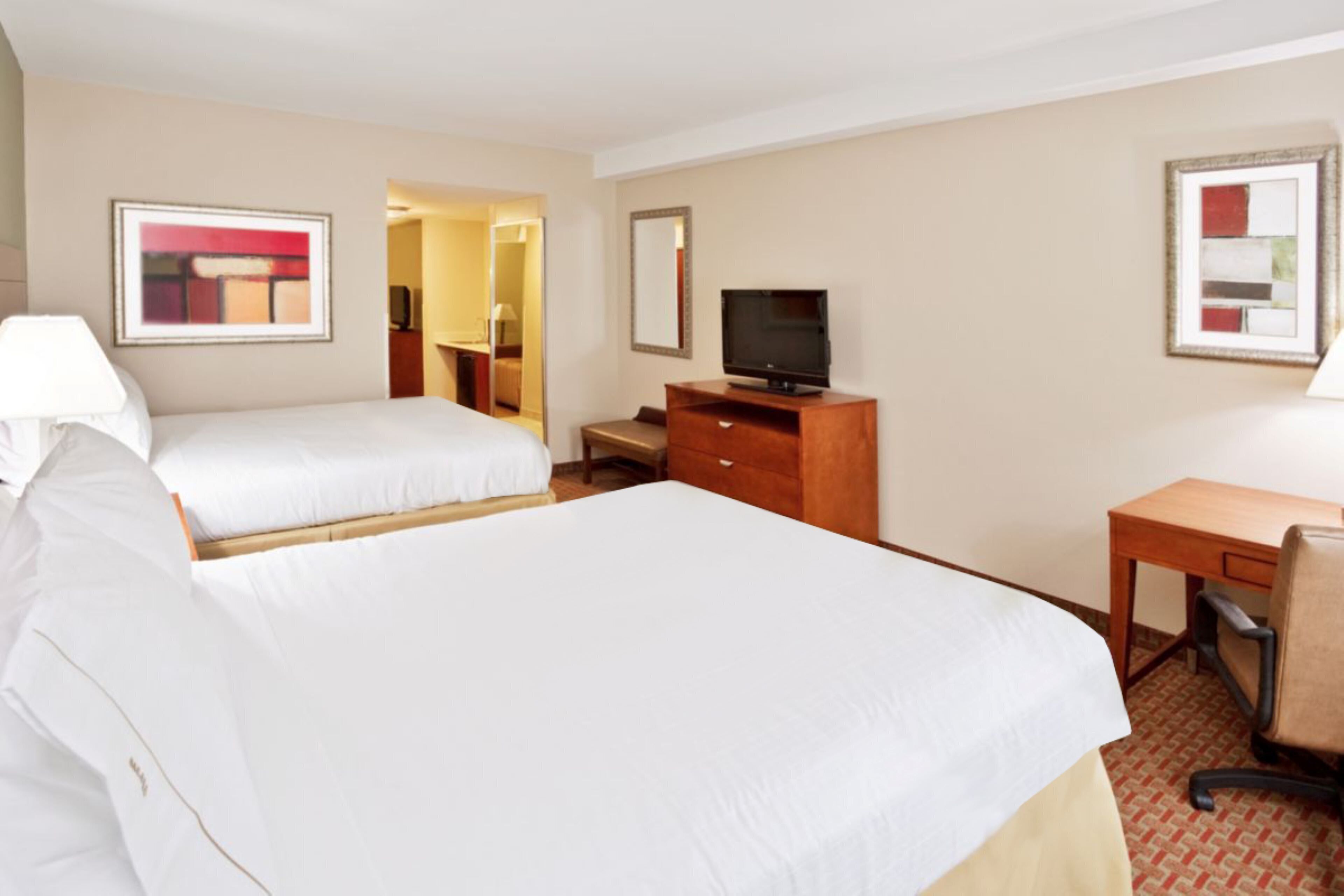 Habitación de hotel con dos camas, televisión, escritorio y una silla.