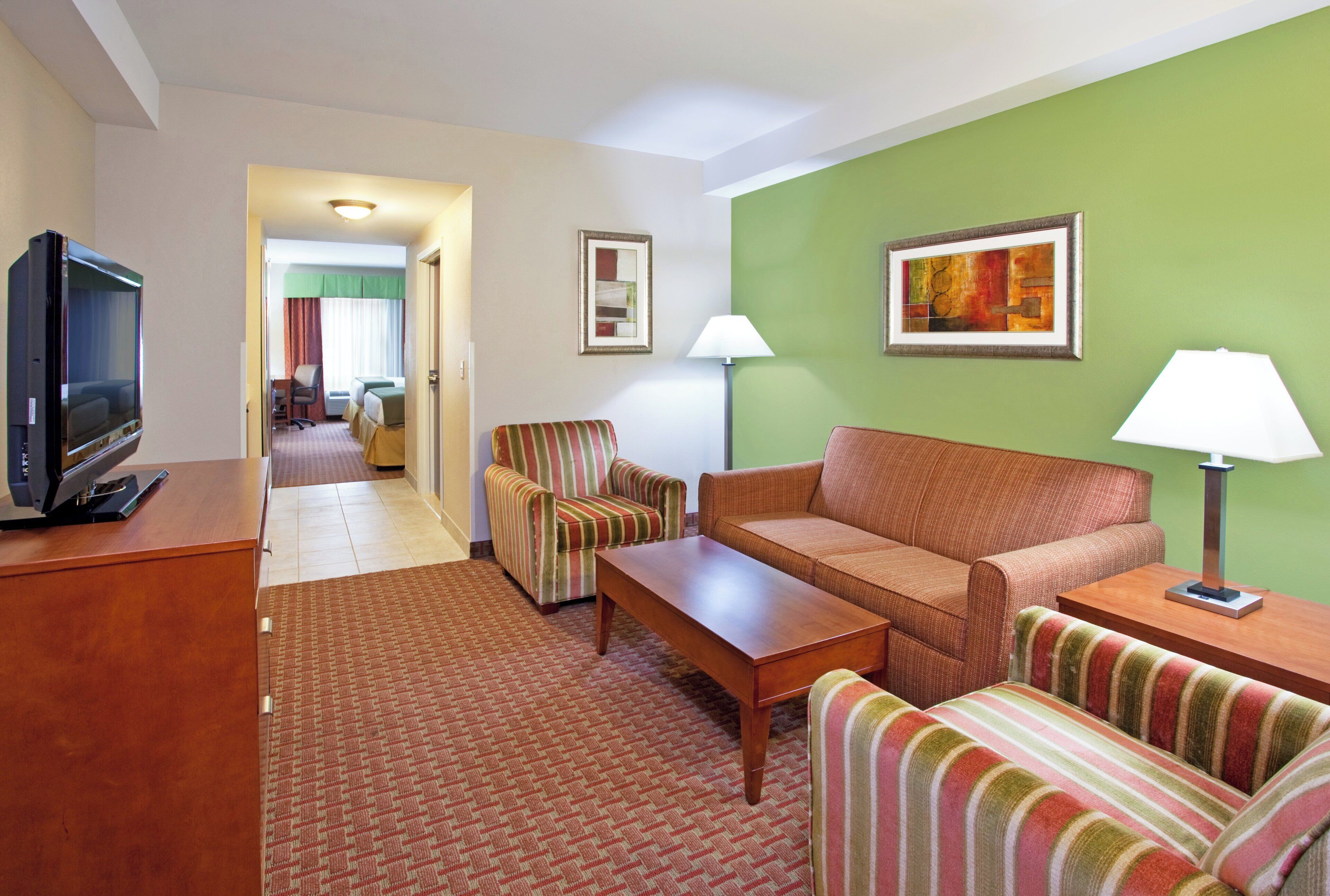 A hotel room with a television, a sofa, a striped armchair, a small table, and two lamps.