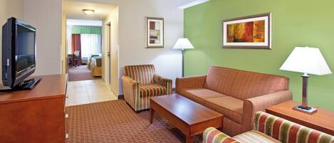 A hotel room with a television, a sofa, a striped armchair, a small table, and two lamps.