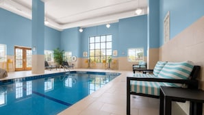 An indoor swimming pool with a tiled floor, a lounge area with chairs and a sofa, and a window with a view of the outdoors. - Holiday Inn Express Hotel & Suites Niagara Falls by IHG (Niagara Falls)