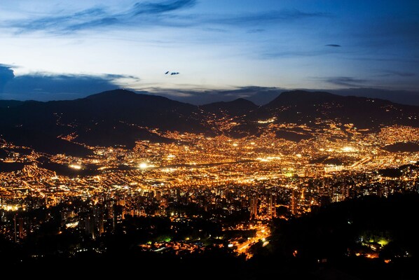 A nighttime cityscape with a dense urban area and distant mountains.