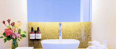 A bathroom with a white sink, a mirror, and a granite countertop. There are bottles of hand soap and lotion, a vase with flowers, and a towel rack with towels.