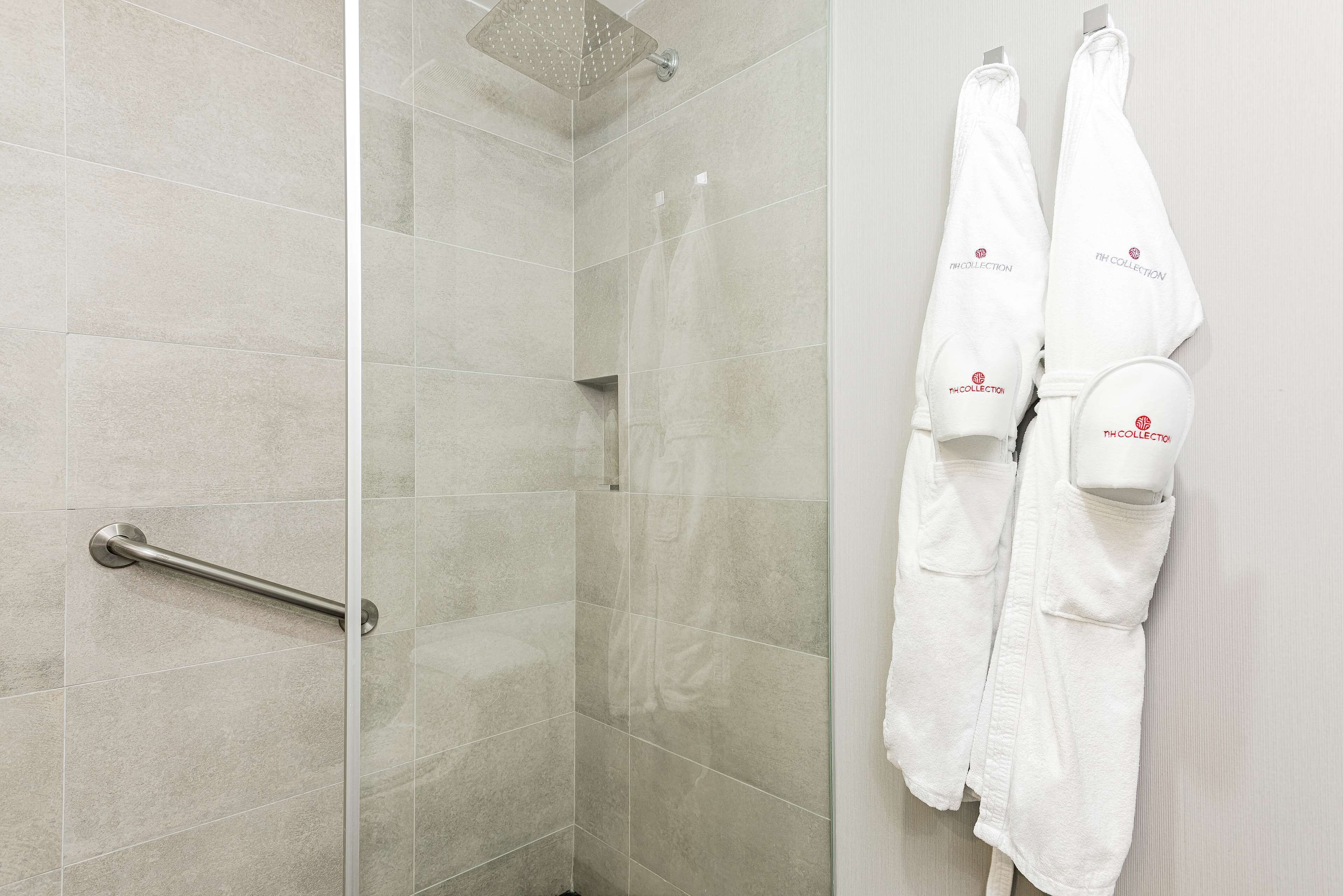 Un bagno moderno con cabina doccia in vetro, un mancorrente e due asciugamani bianchi appesi a una parete.