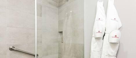 Un baño moderno con mampara de vidrio, un pasamanos y dos toallas blancas colgadas en la pared.