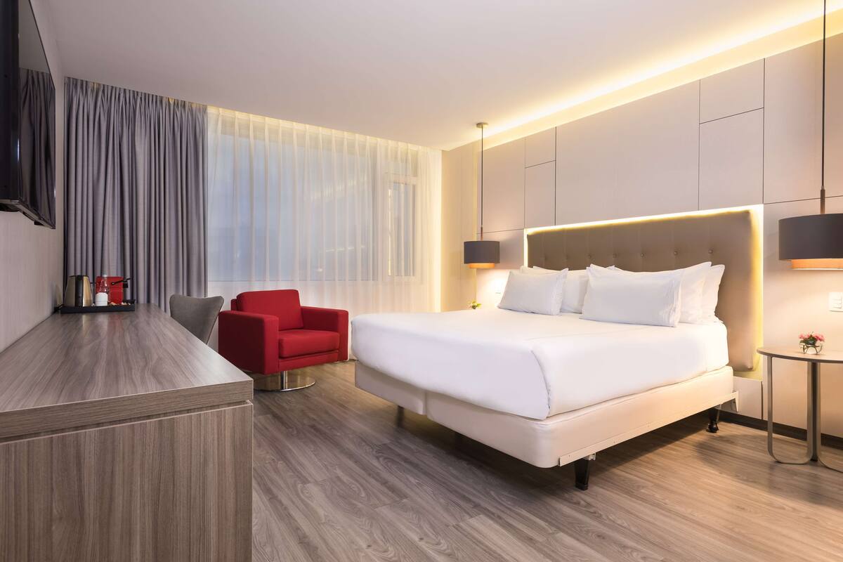 Moderni hotellihuone, jossa on suuri sänky, punainen tuoli, työpöytä ja televisio.