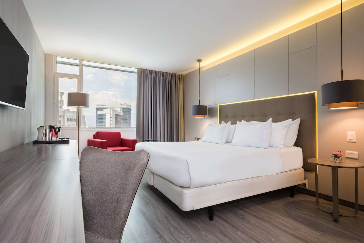 Moderni hotellihuone, jossa on suuri sänky, punainen tuoli, pieni pöytä ja televisio.