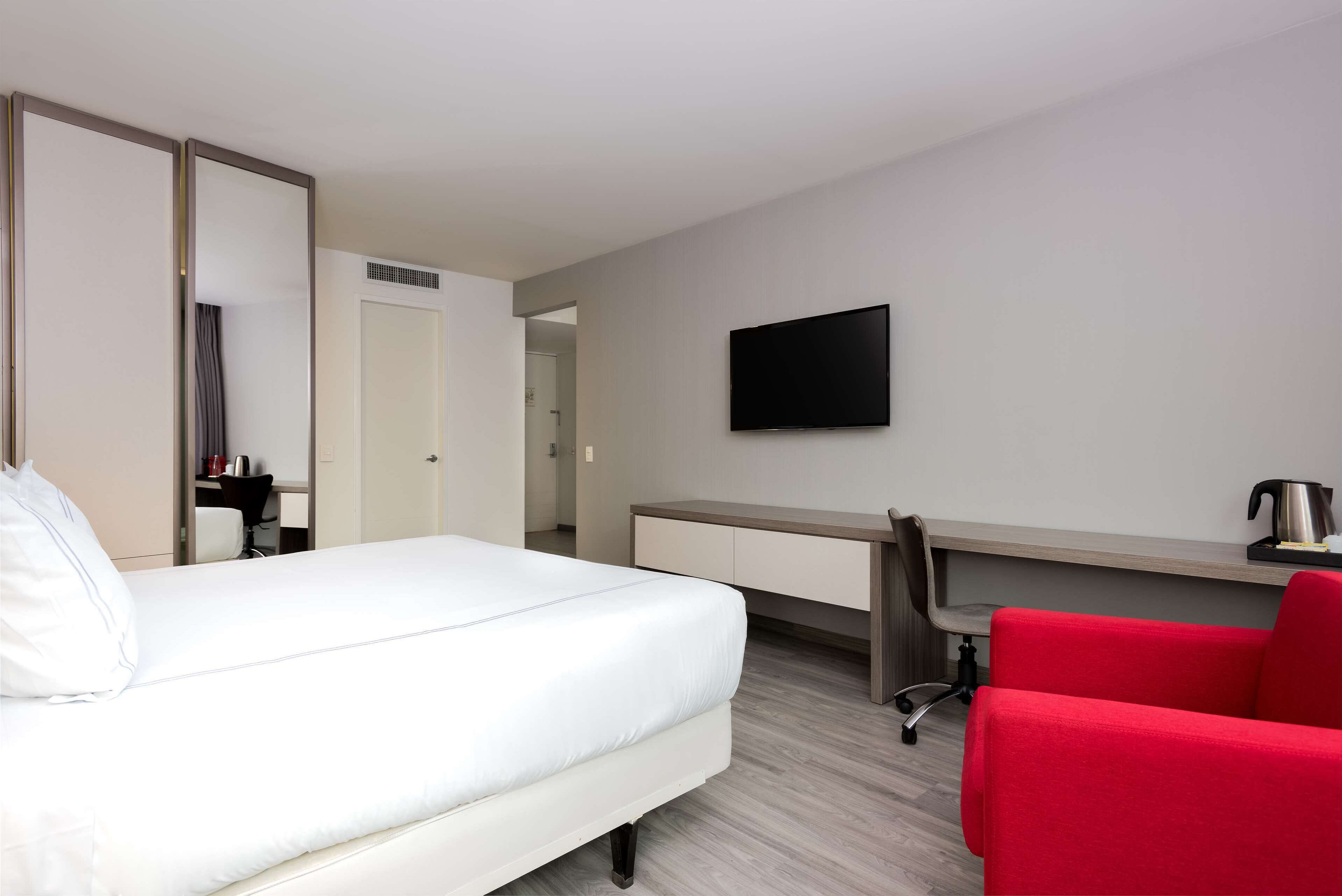 Habitación de hotel con cama, escritorio, silla, televisor y armario.