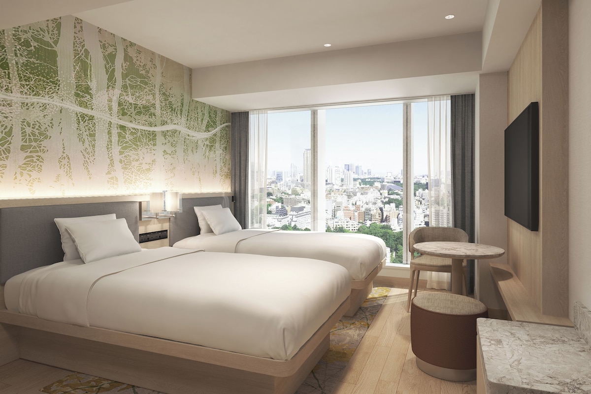 A modern hotel room with two beds, a city view, a flat-screen TV, and a small round table.
