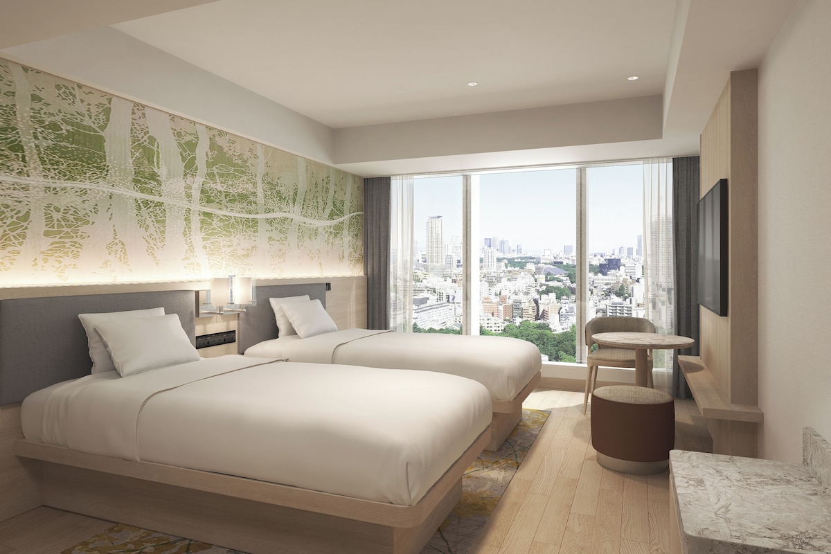 A modern hotel room with two beds, a city view, a round table, and a marble countertop.