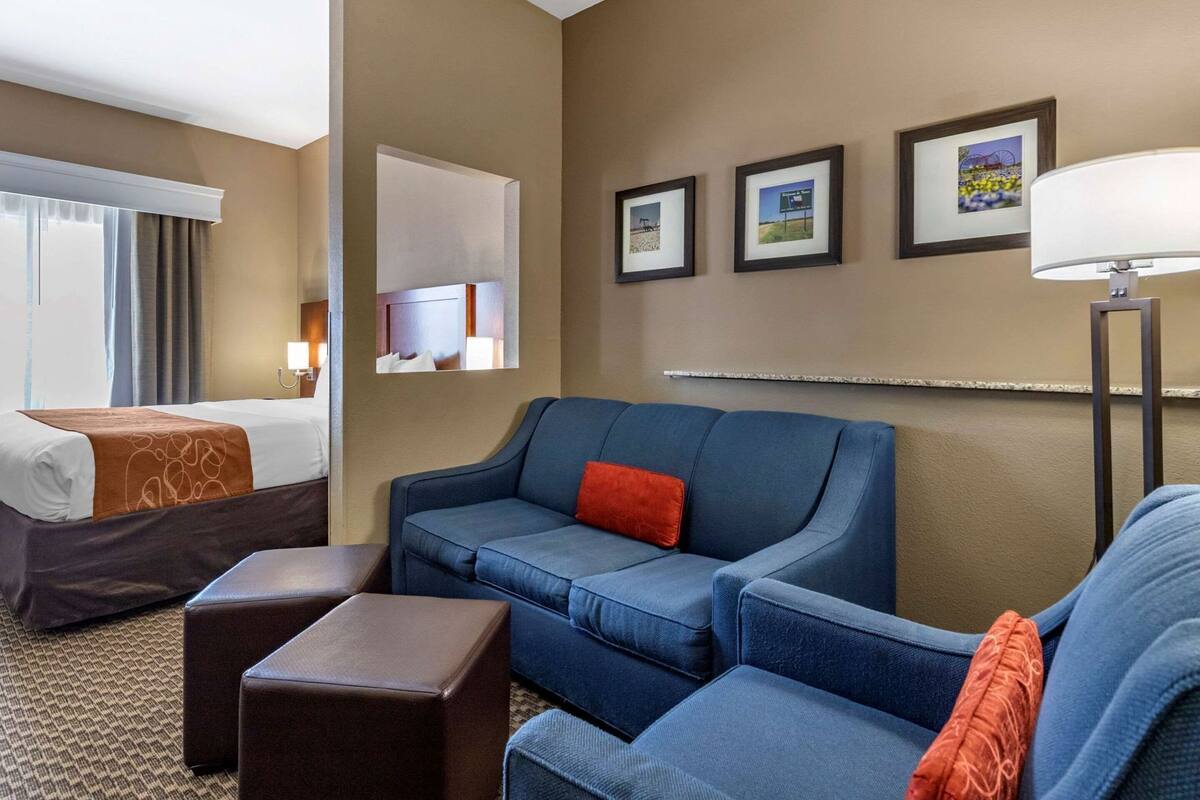 Una habitación de hotel con una cama, un sofá azul, una mesita y una lámpara.