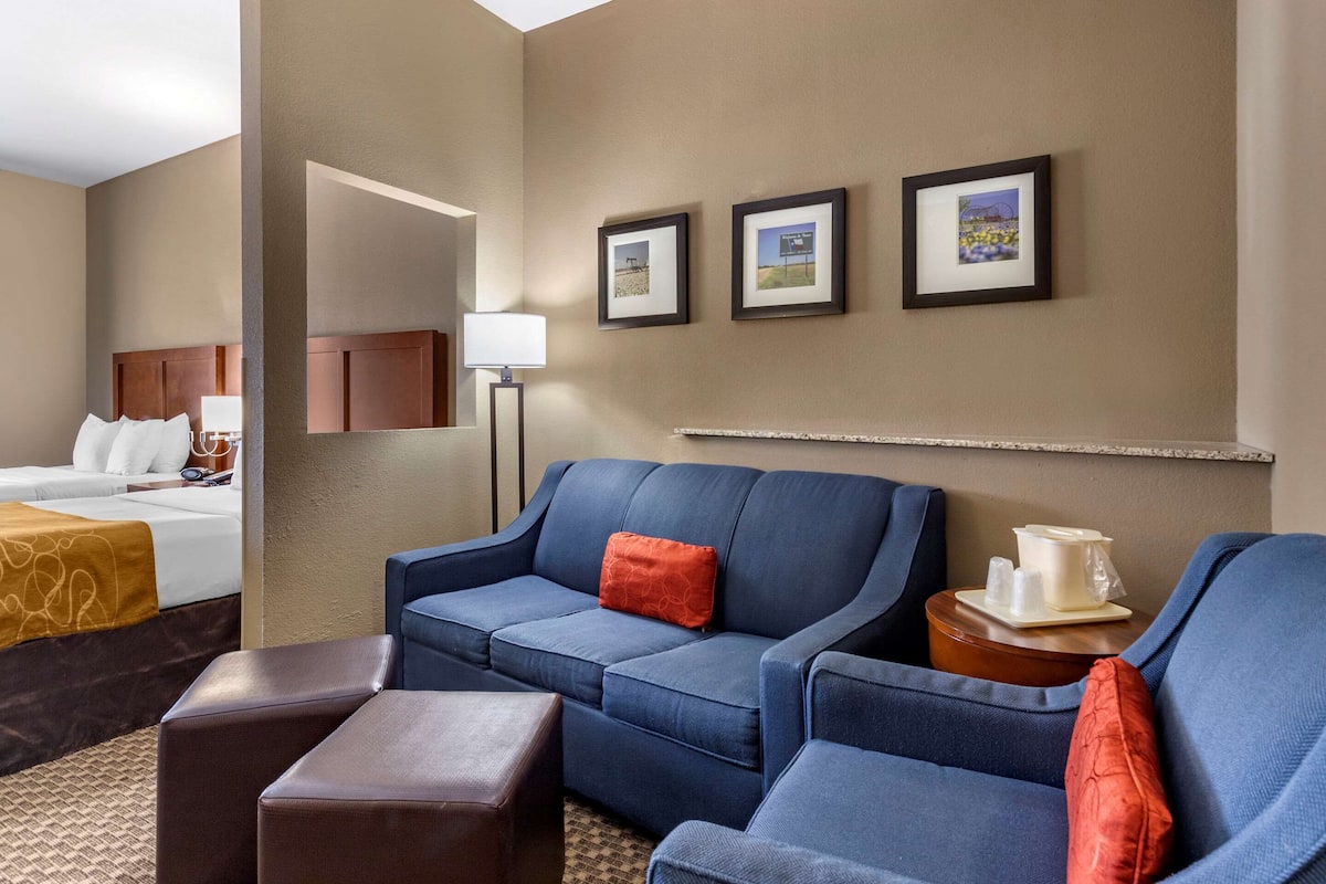 Una habitación de hotel con una cama, un sofá azul, una mesita de madera con una jofaina blanca y cuadros enmarcados en la pared.