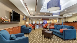 A hotel lobby with blue sofas, a patterned carpet, and a large TV screen. - Comfort Suites Near Texas A&M University - Corpus Christi (Corpus Christi)