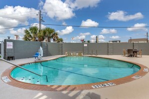 Una piscina con borde de azulejos, una silla de socorrista y una pequeña mesa con sillas.