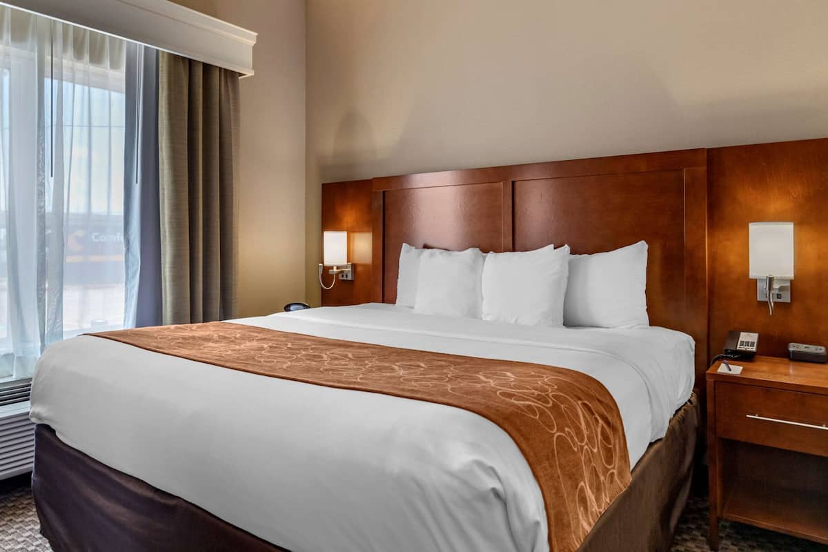 Habitación de hotel con una cama grande, un cabecero de madera, dos lámparas de noche, una mesita de noche y una ventana con cortinas.