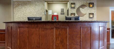A reception desk with a wooden finish, a stone wall backdrop, and a recessed ceiling with lighting.