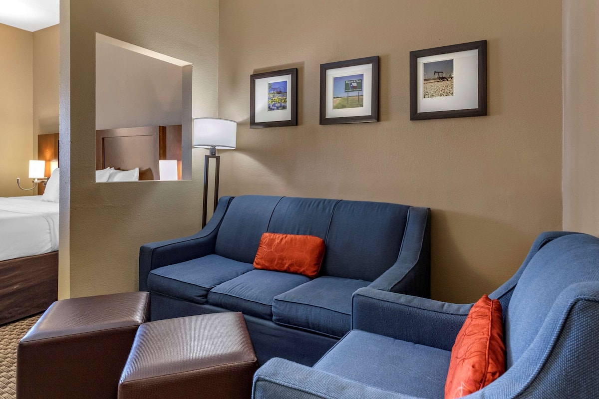 Una habitación de hotel con un sofá azul, dos otomanas marrones, una cama y tres cuadros en la pared.