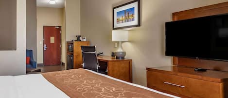 A hotel room with a bed, a desk, a chair, a television, and a lamp.