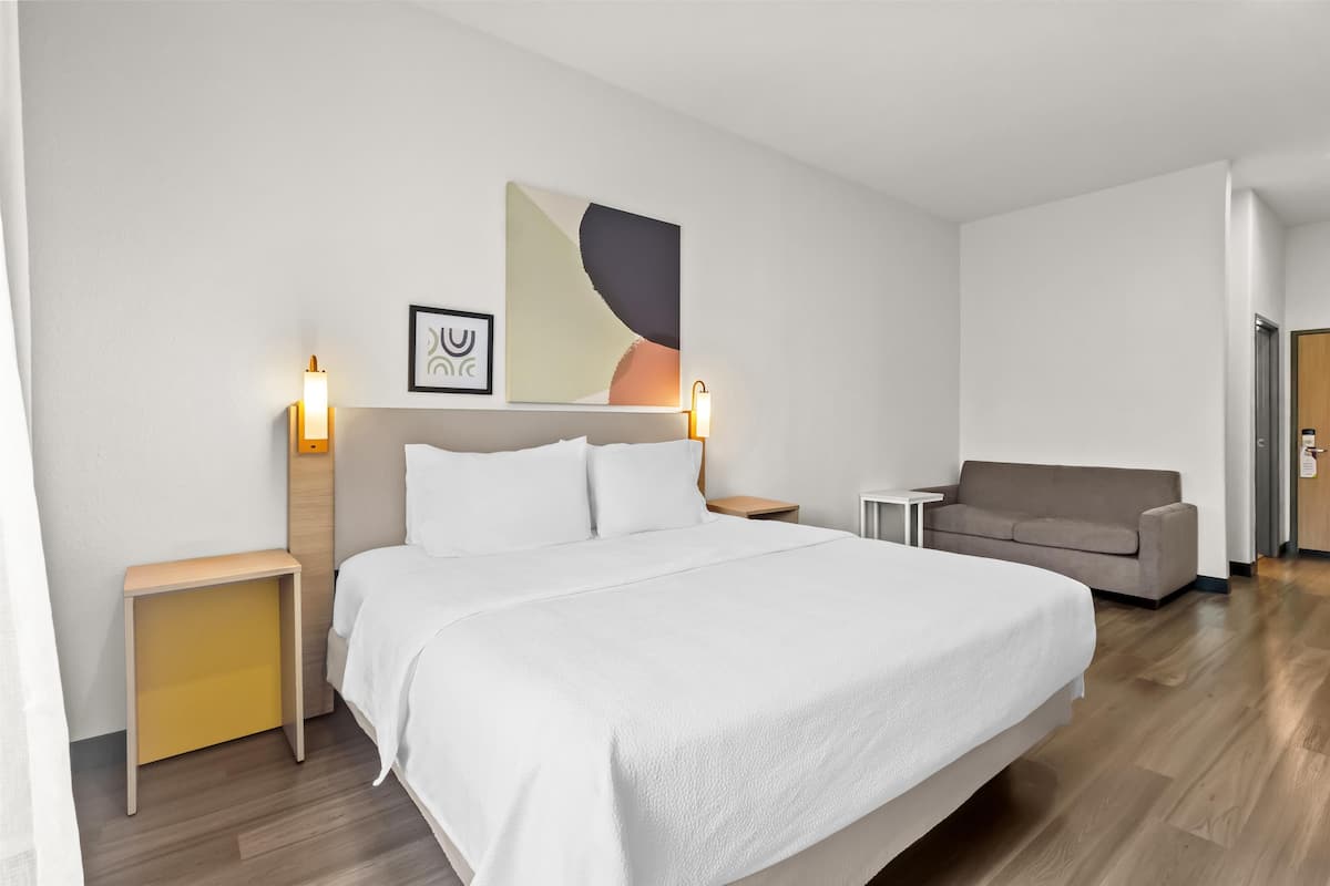 Une chambre d’hôtel avec un grand lit, un canapé, une petite table et deux lampes fixées au mur.
