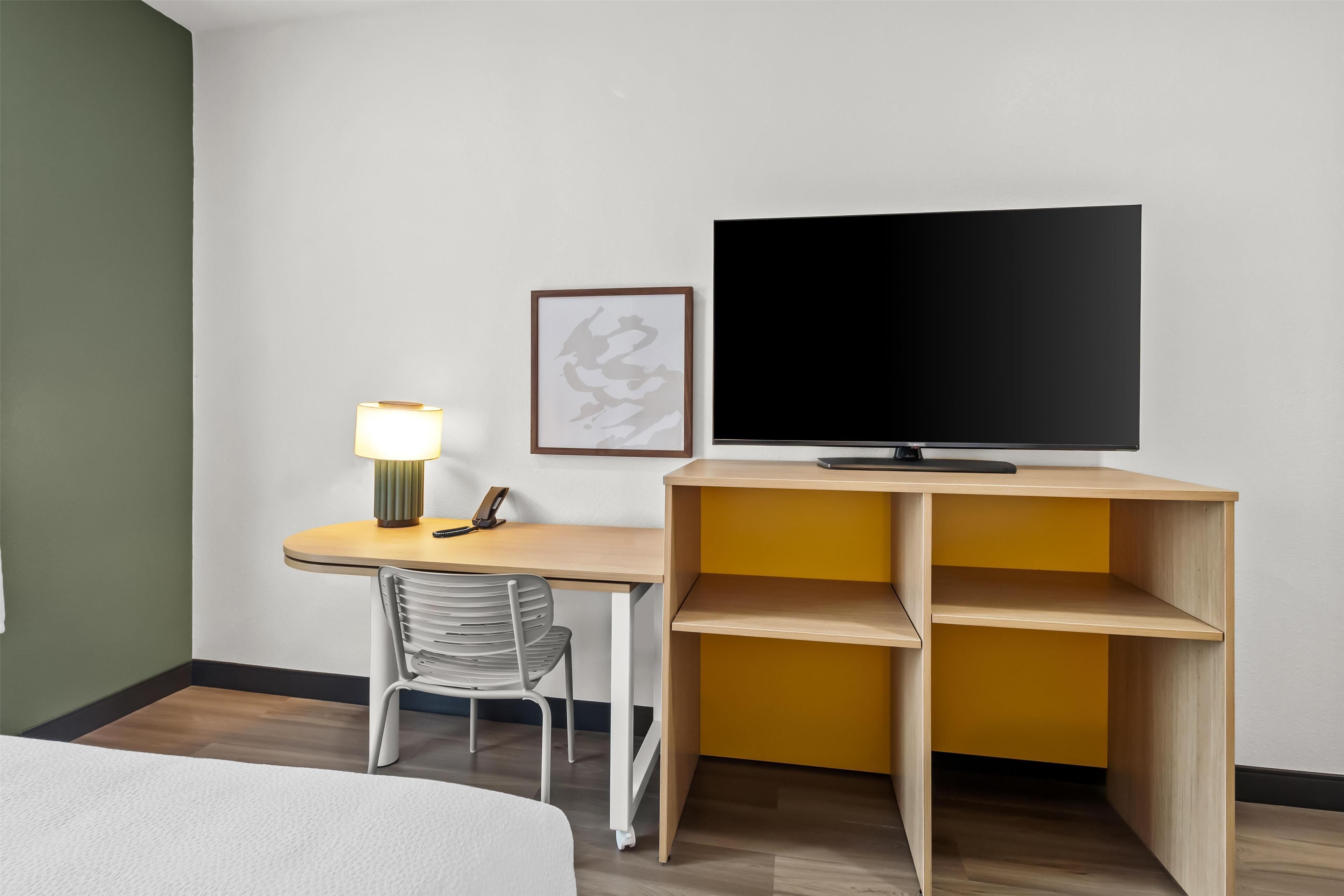 Une chambre d’hôtel avec un lit, un bureau doté d’une lampe, une chaise, un téléviseur et un tableau encadré au mur.