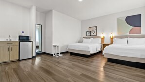 A hotel room with two beds, a small kitchenette, a microwave, and a large abstract painting on the wall.