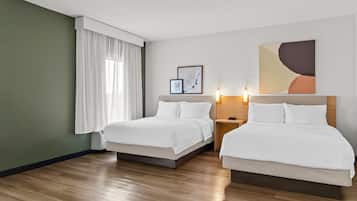A hotel room with two beds, a nightstand, a wall-mounted artwork, and a window with white curtains.