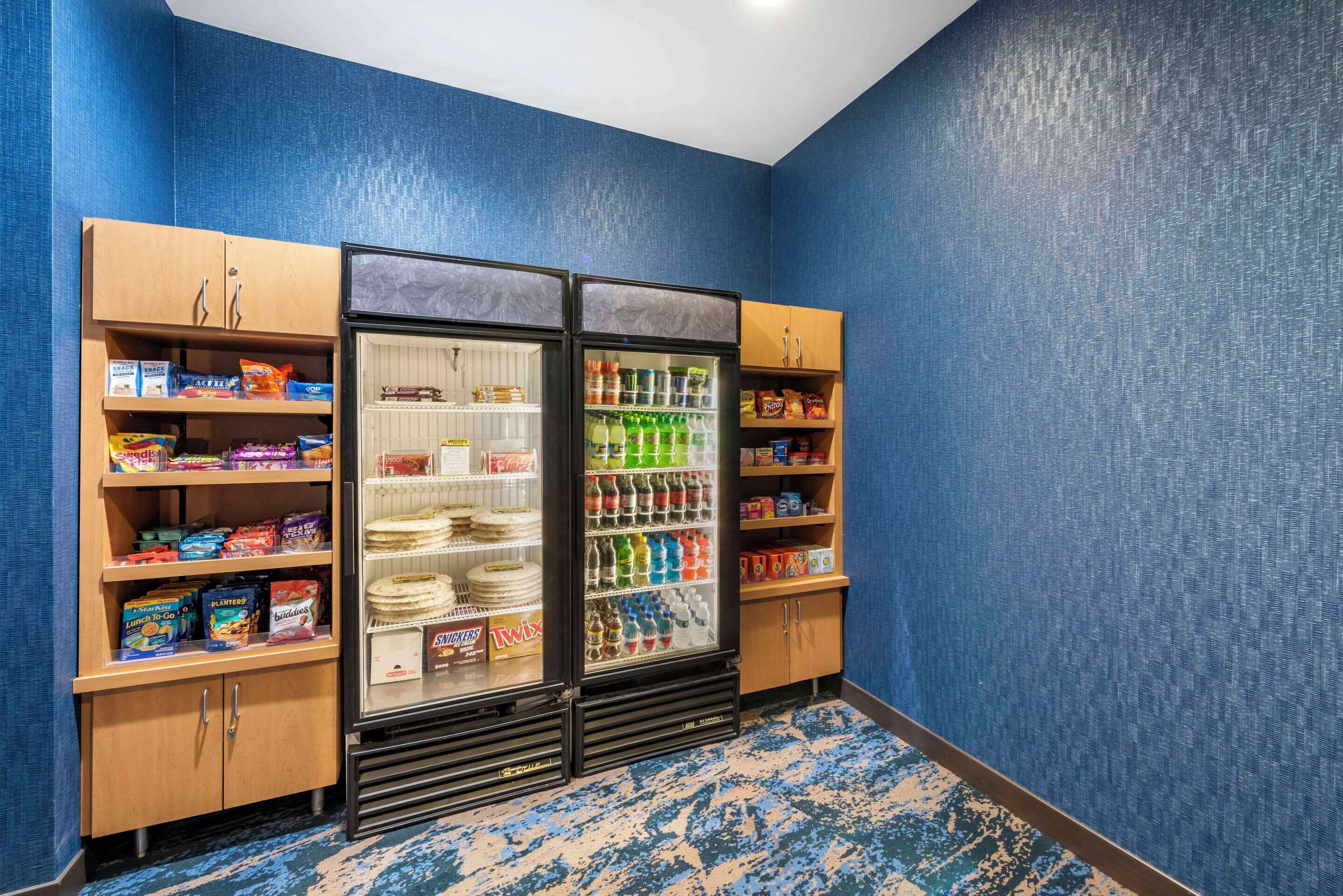 Une pièce avec un mur bleu à texture, une moquette bleue à motifs et un réfrigérateur rempli de boissons et d’en-cas.