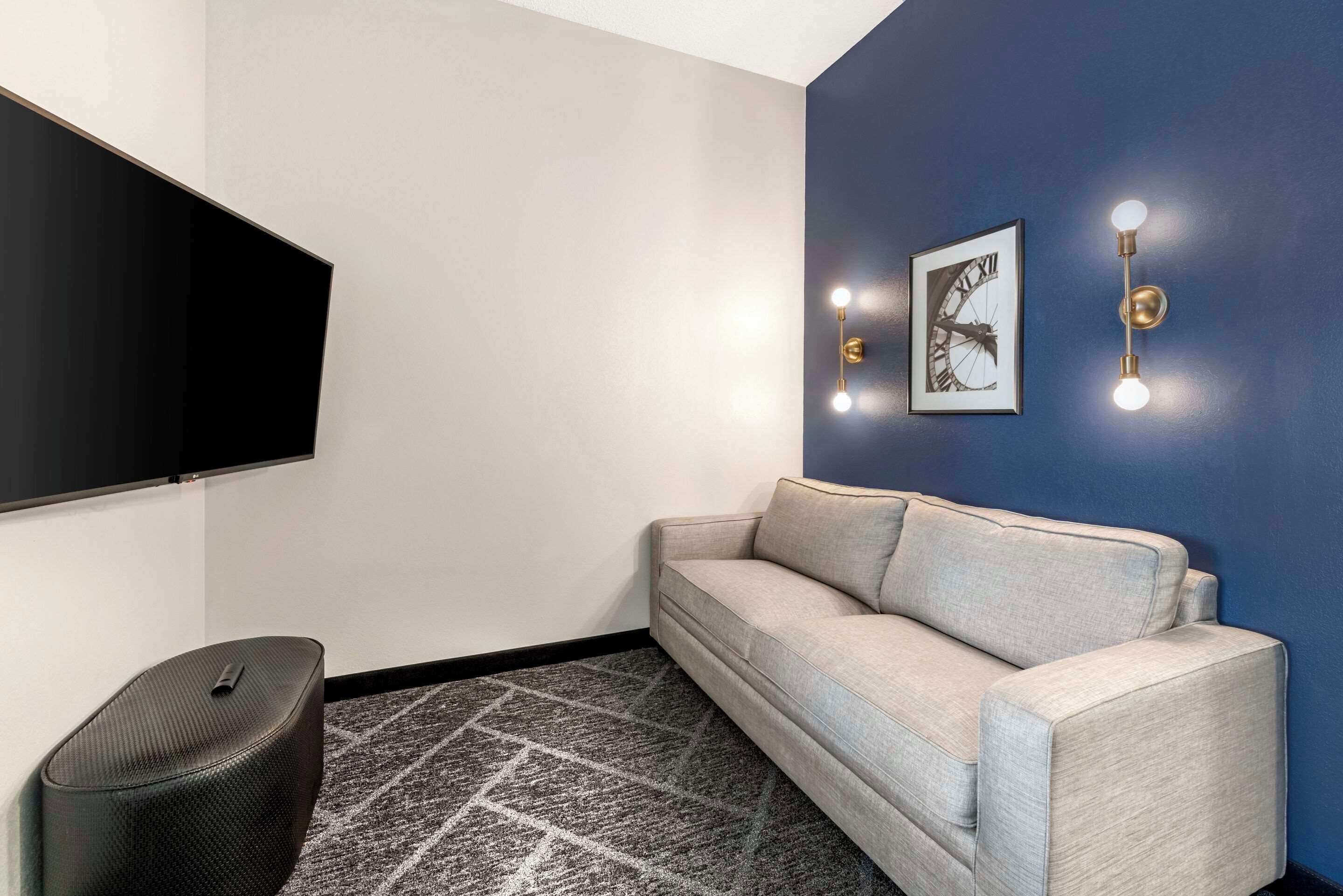 Un salon moderne doté d’un téléviseur à écran plat, d’un canapé de couleur claire, d’un tapis à motifs et d’un luminaire fixé au mur.