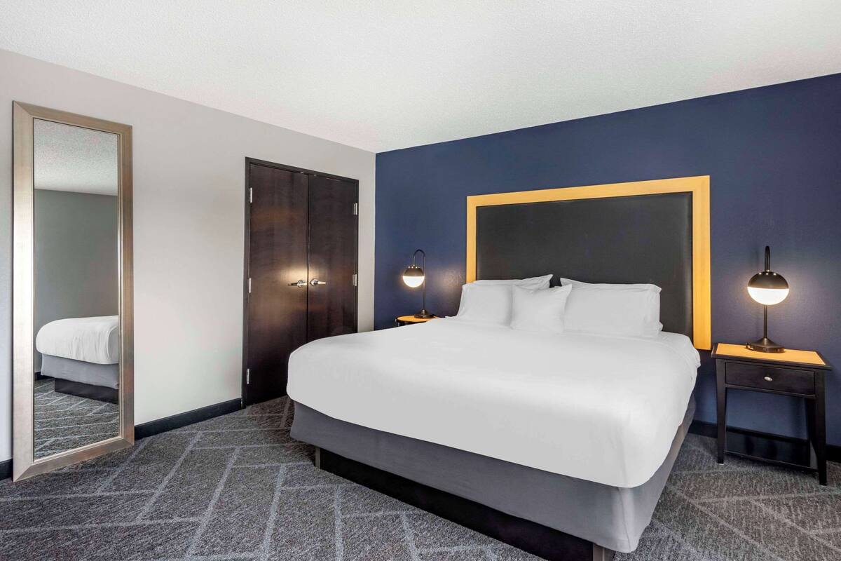Habitación de hotel con una cama grande, un cabecero azul oscuro, un armario de madera y dos lámparas de noche.
