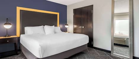 Una habitación de hotel con una cama grande, un armario oscuro, un espejo y una mesita de noche con una lámpara.