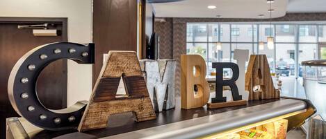A reception desk with large wooden letters spelling "CAMBRIA" and various packaged food items on display.