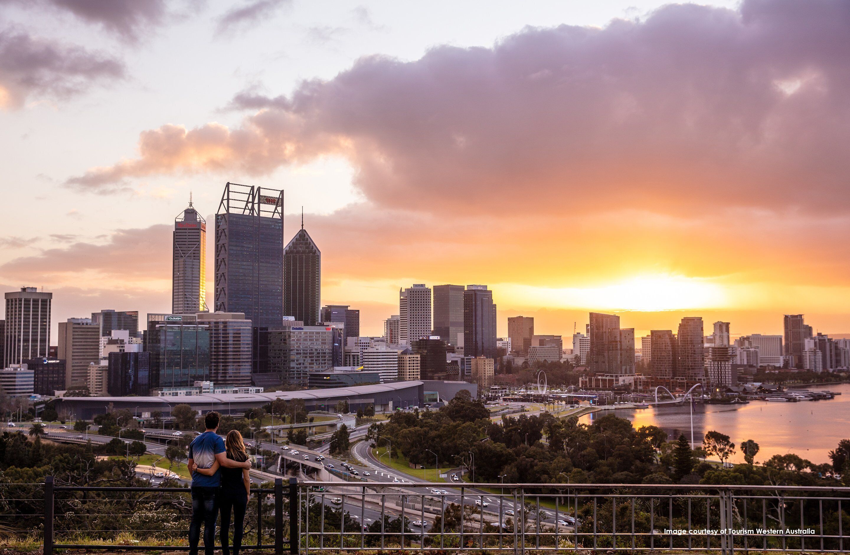 A city skyline at sunset with modern buildings and a river.