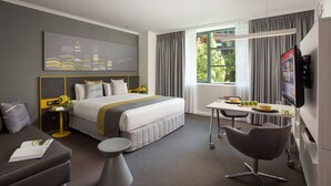 Habitación de hotel moderna con una cama grande, un escritorio con silla, televisión y vistas a zonas verdes.
