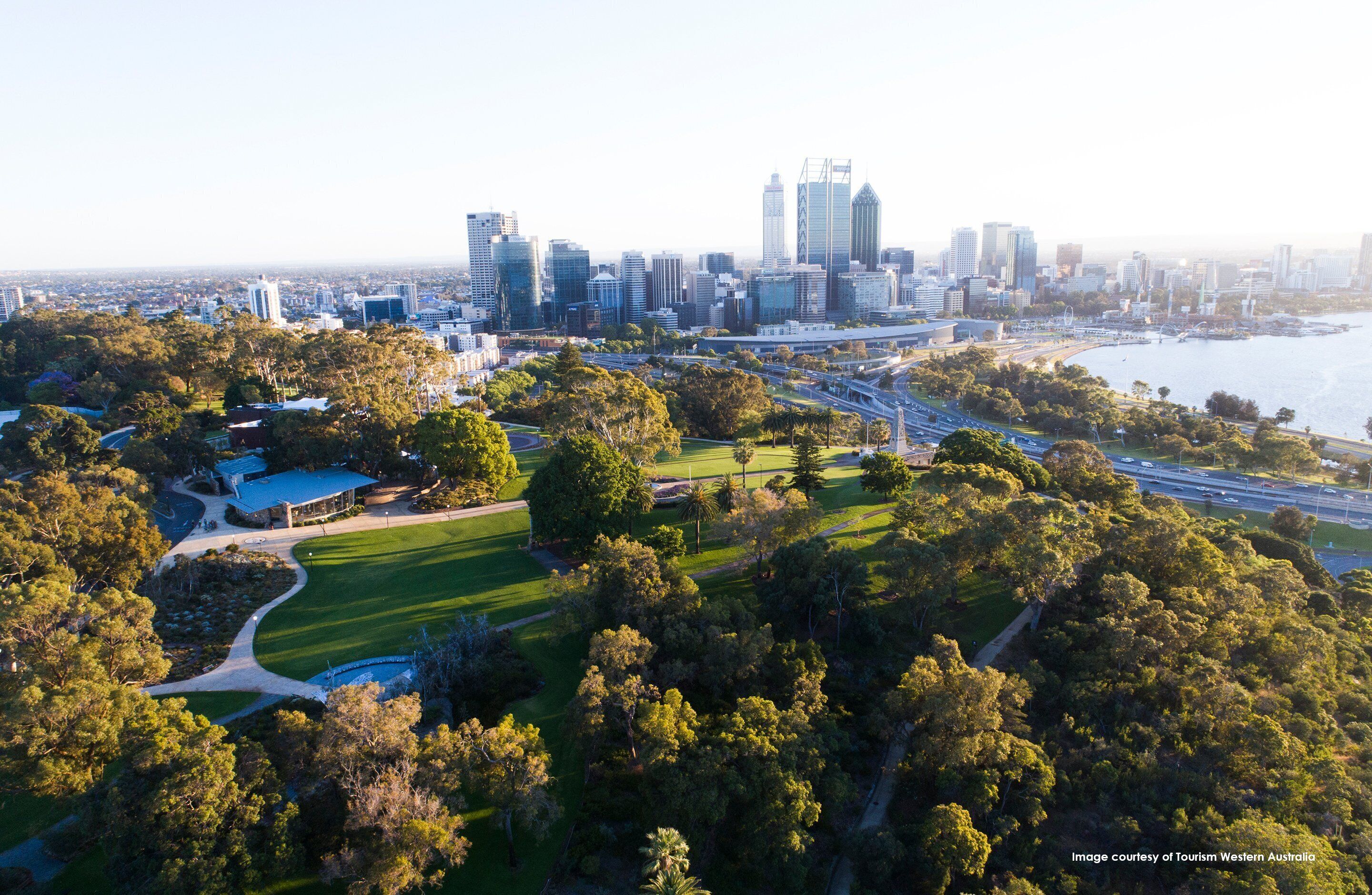 An aerial view of a city with a prominent skyline, a large park with pathways, and a body of water.