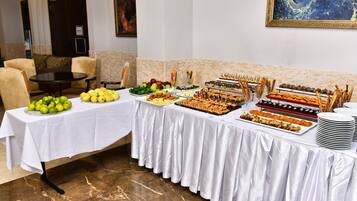 Uma mesa de buffet com diversos alimentos, um quadro na parede e uma área de estar com cadeiras.