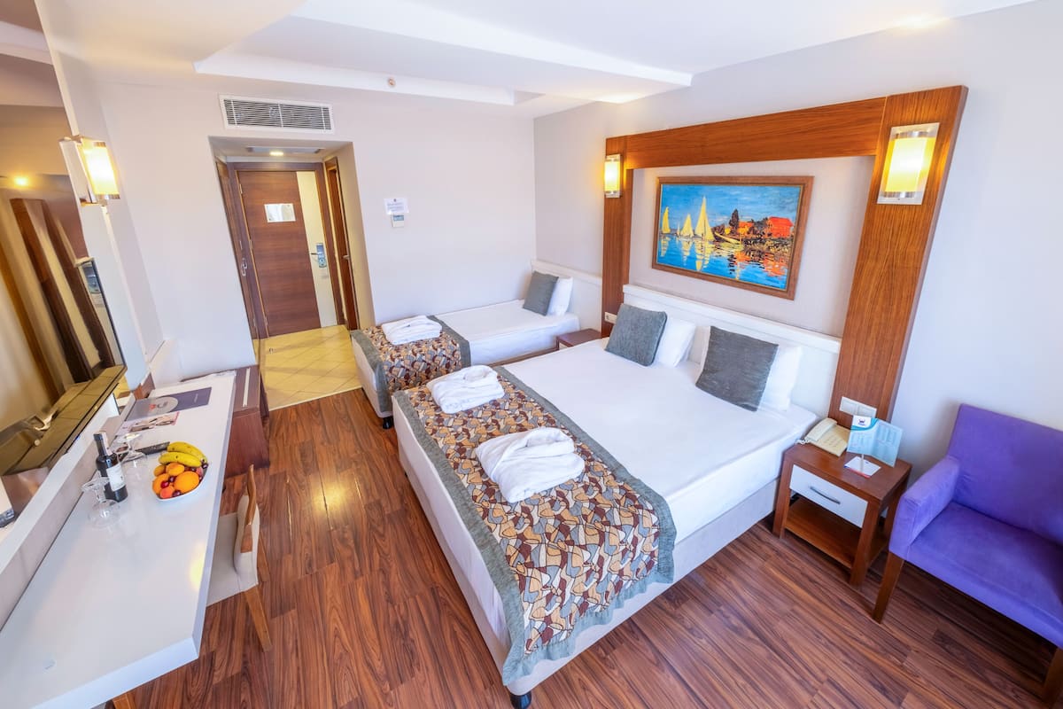 Habitación de hotel con dos camas, piso de madera, un escritorio con frutero, un cuadro en la pared y una silla morada.