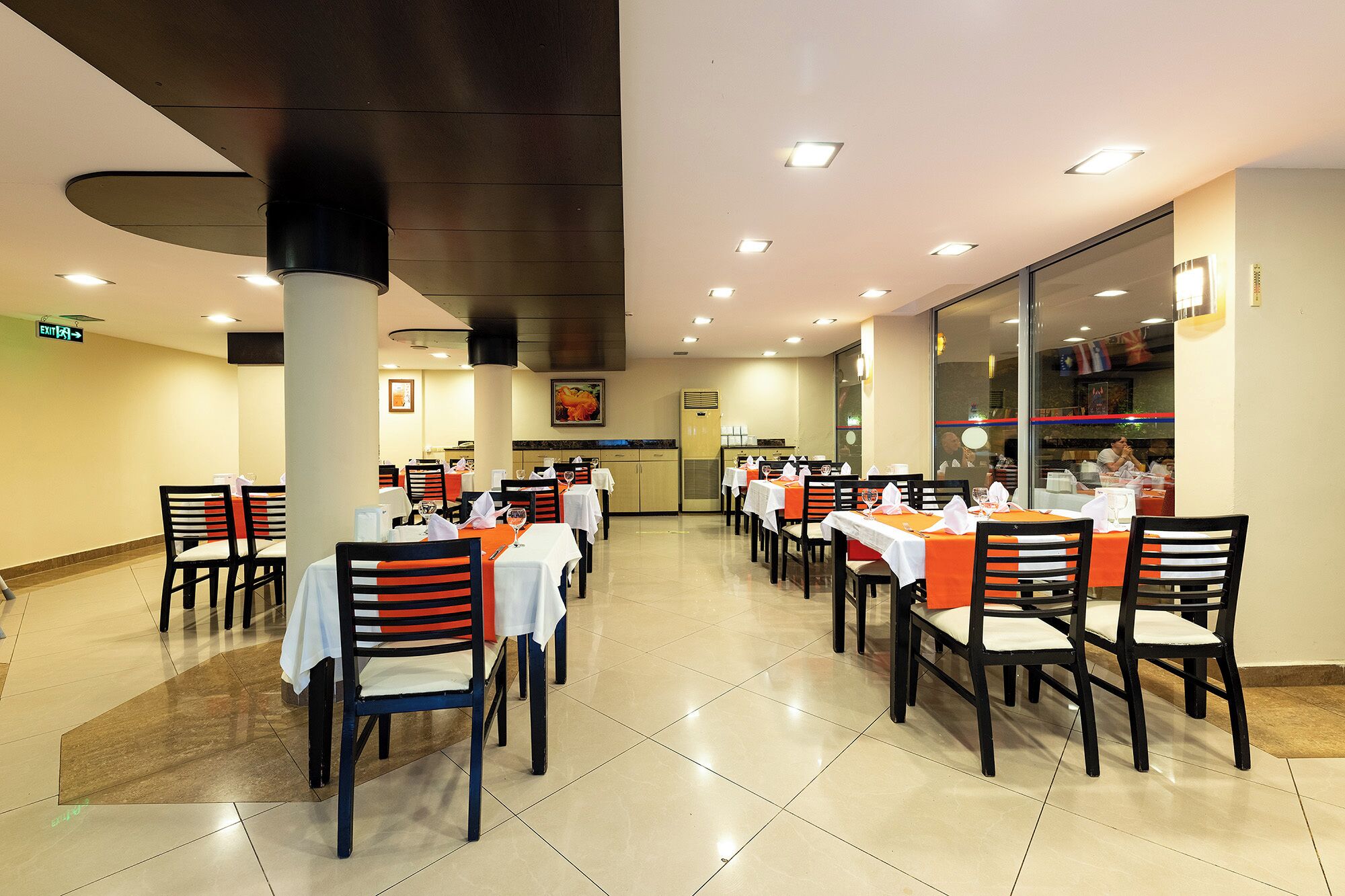 A restaurant with multiple tables and chairs, a tiled floor, and a ceiling with recessed lighting.