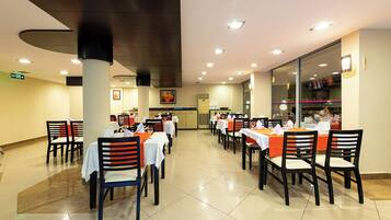 A restaurant with multiple tables and chairs, a tiled floor, and a ceiling with recessed lighting.