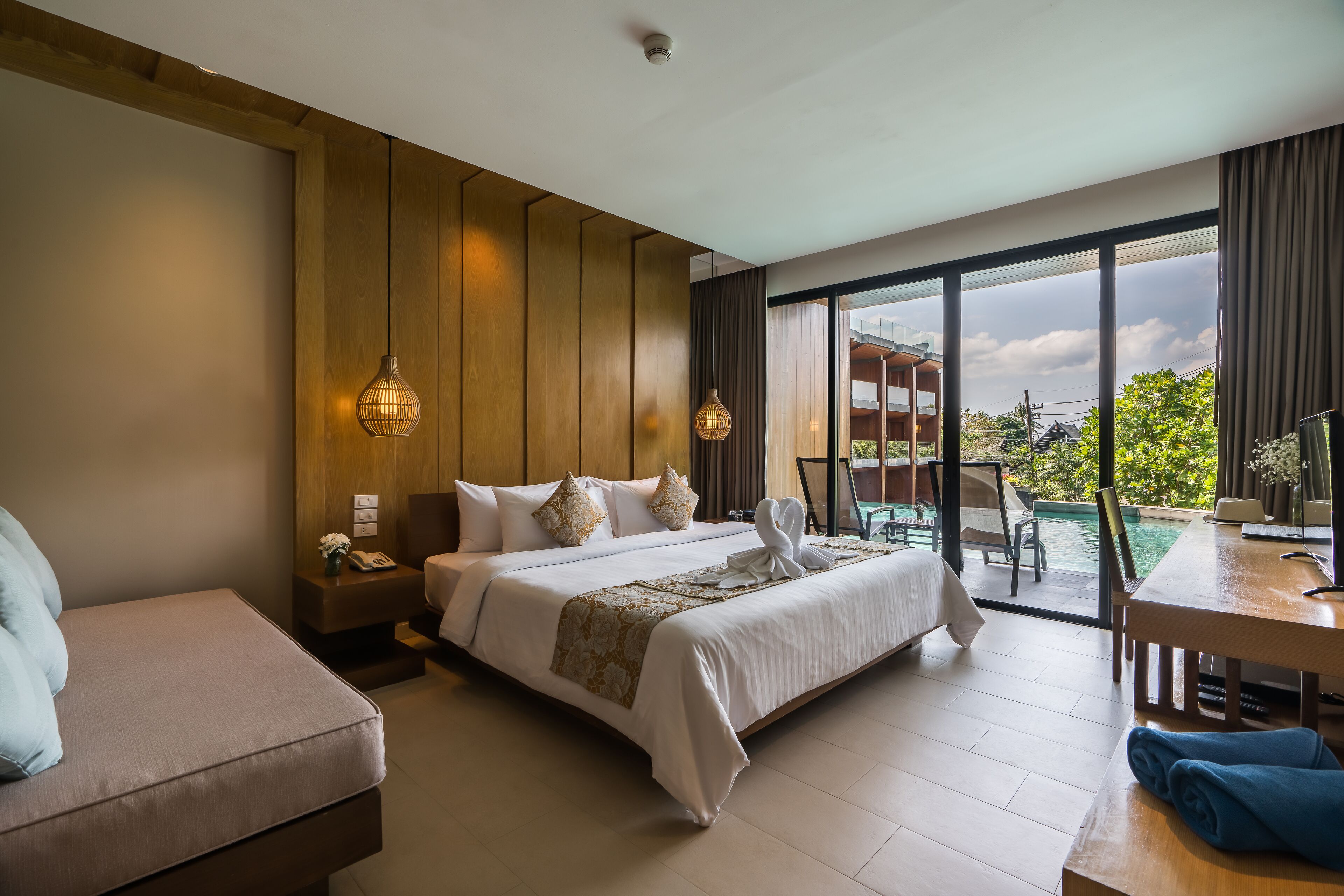A hotel room with a large bed, a sitting area, a dining table, and a view of a pool and greenery outside.