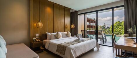A hotel room with a large bed, a sitting area, a dining table, and a view of a pool and greenery outside.