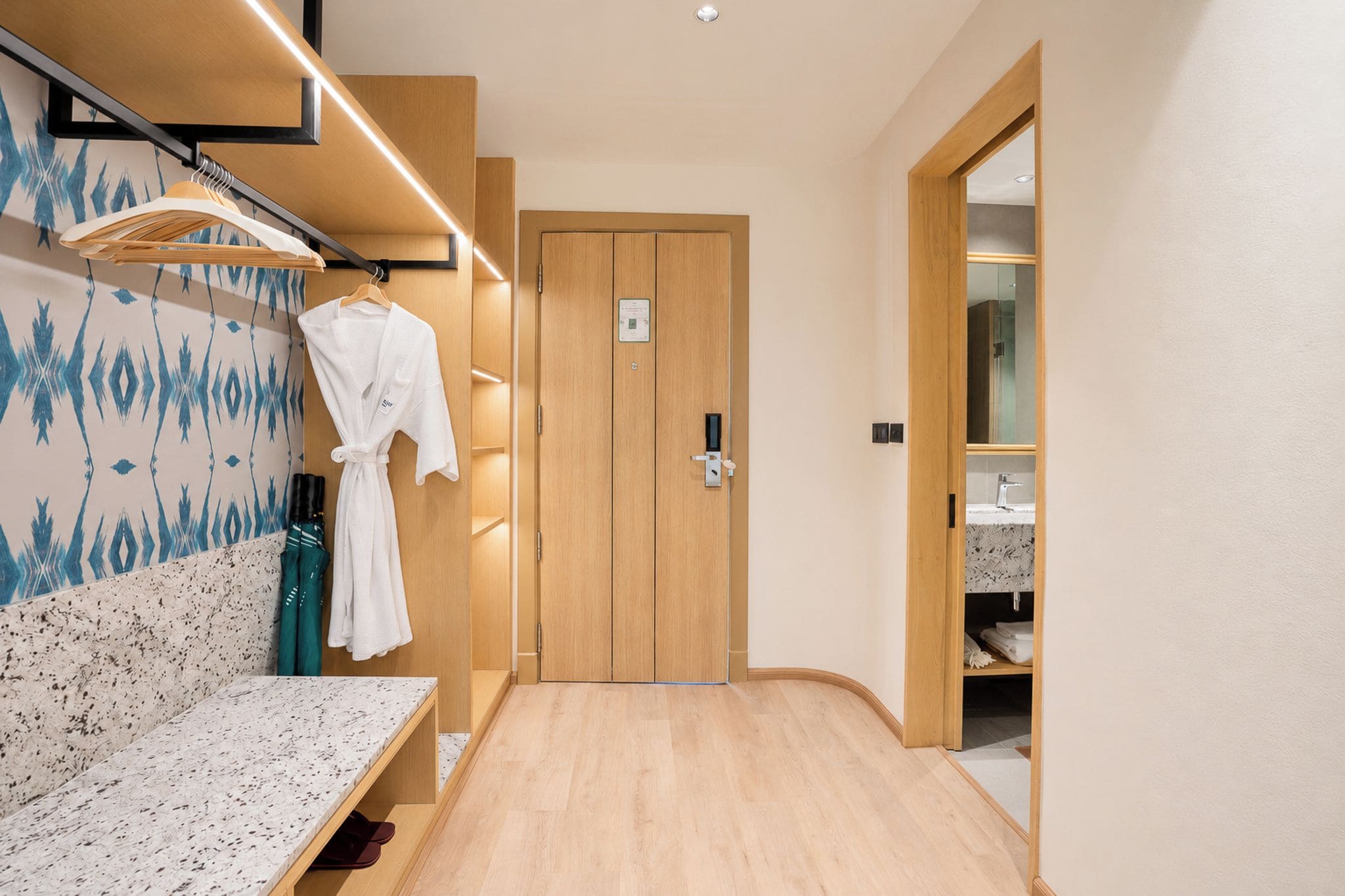 A hotel bathroom with a wooden bench, a robe hanging on a rack, and a wooden door.