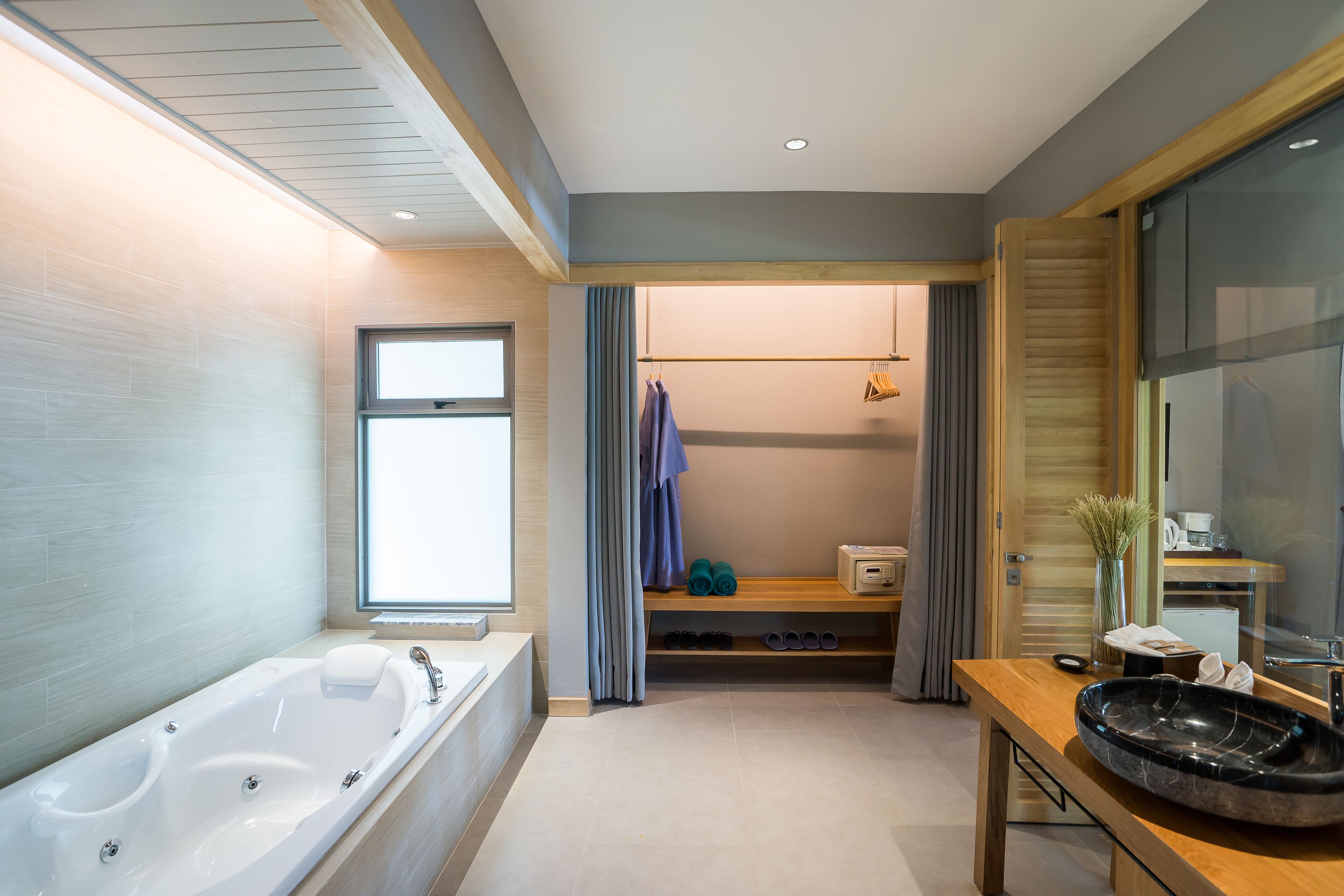 A modern bathroom with a large bathtub, a wooden vanity with a black basin, and a window providing natural light.