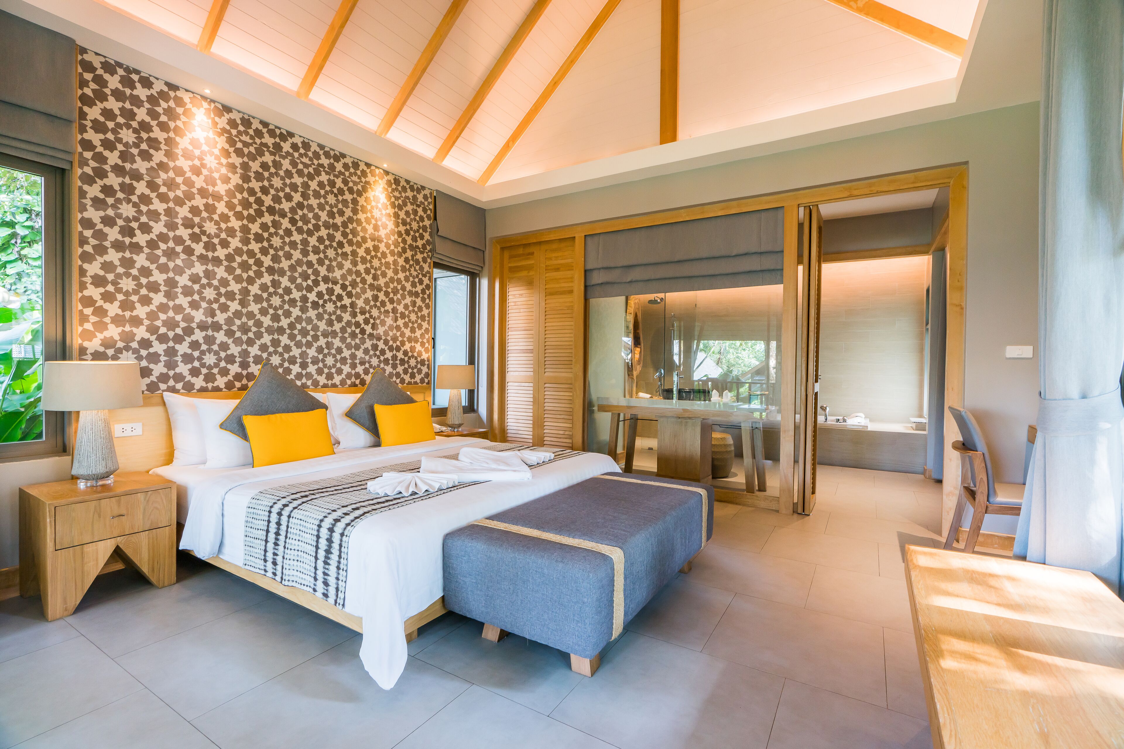Een moderne slaapkamer met een groot bed, een bureau en een zichtbare badkamer door een glazen deur.