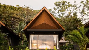 Une villa moderne dotée d’un toit triangulaire, de grandes fenêtres et d’une végétation luxuriante qui l’entoure.